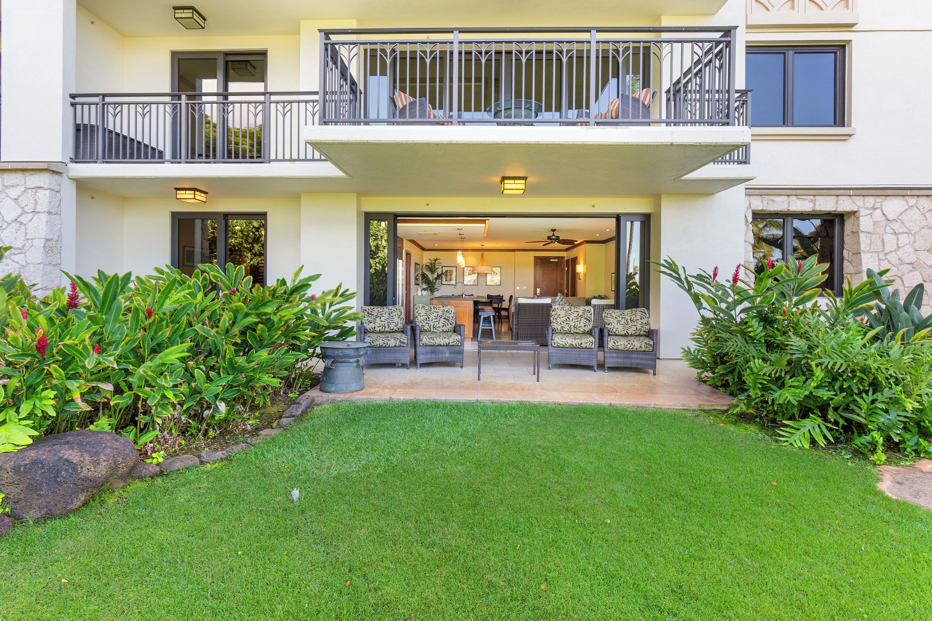 A two-story residential building with a balcony, outdoor seating area, and a well-maintained lawn.