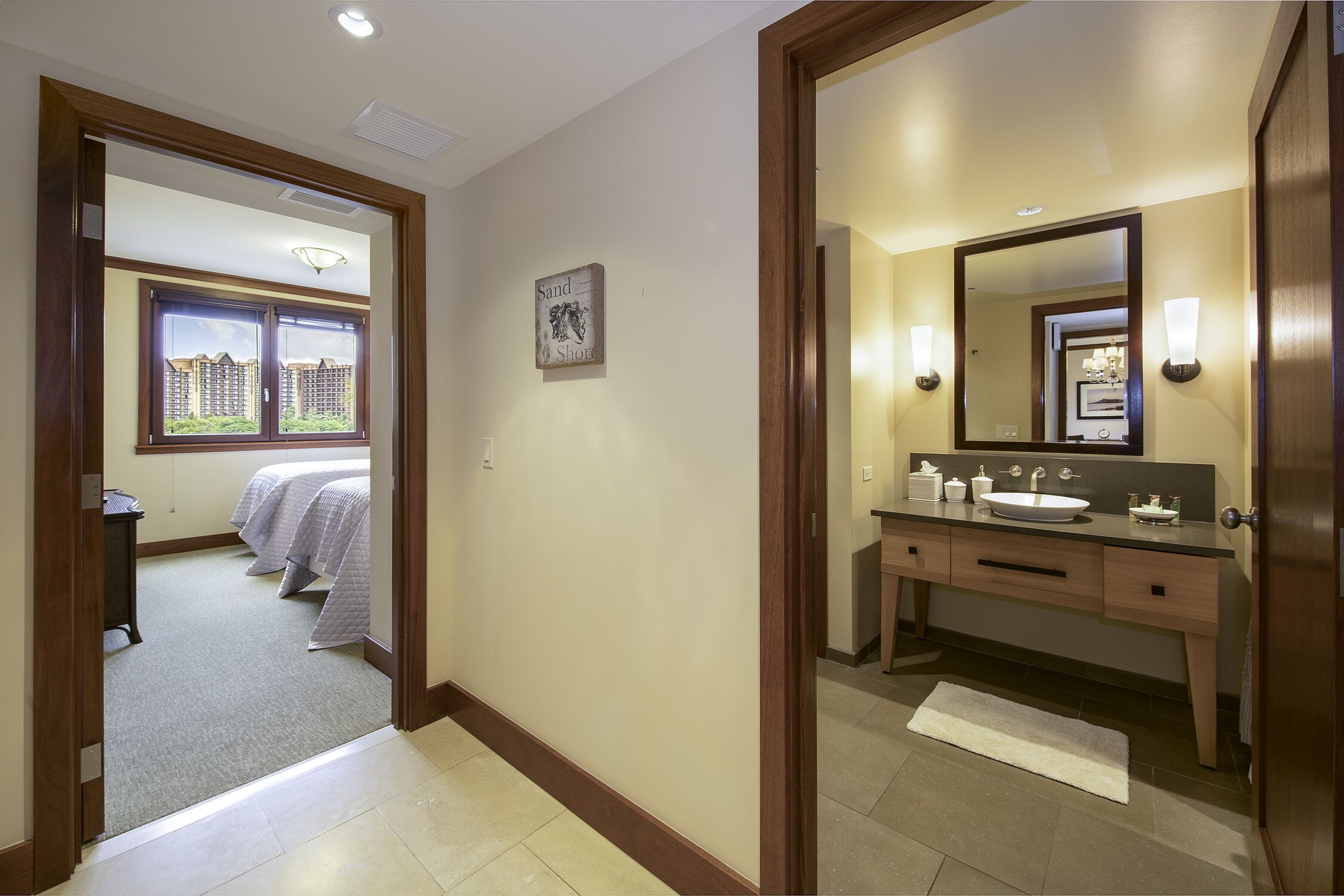 A hotel room with a bed, a bathroom with a sink and mirror, and a view of buildings outside the window.