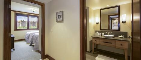 A hotel room with a bed, a bathroom with a sink and mirror, and a view of buildings outside the window.