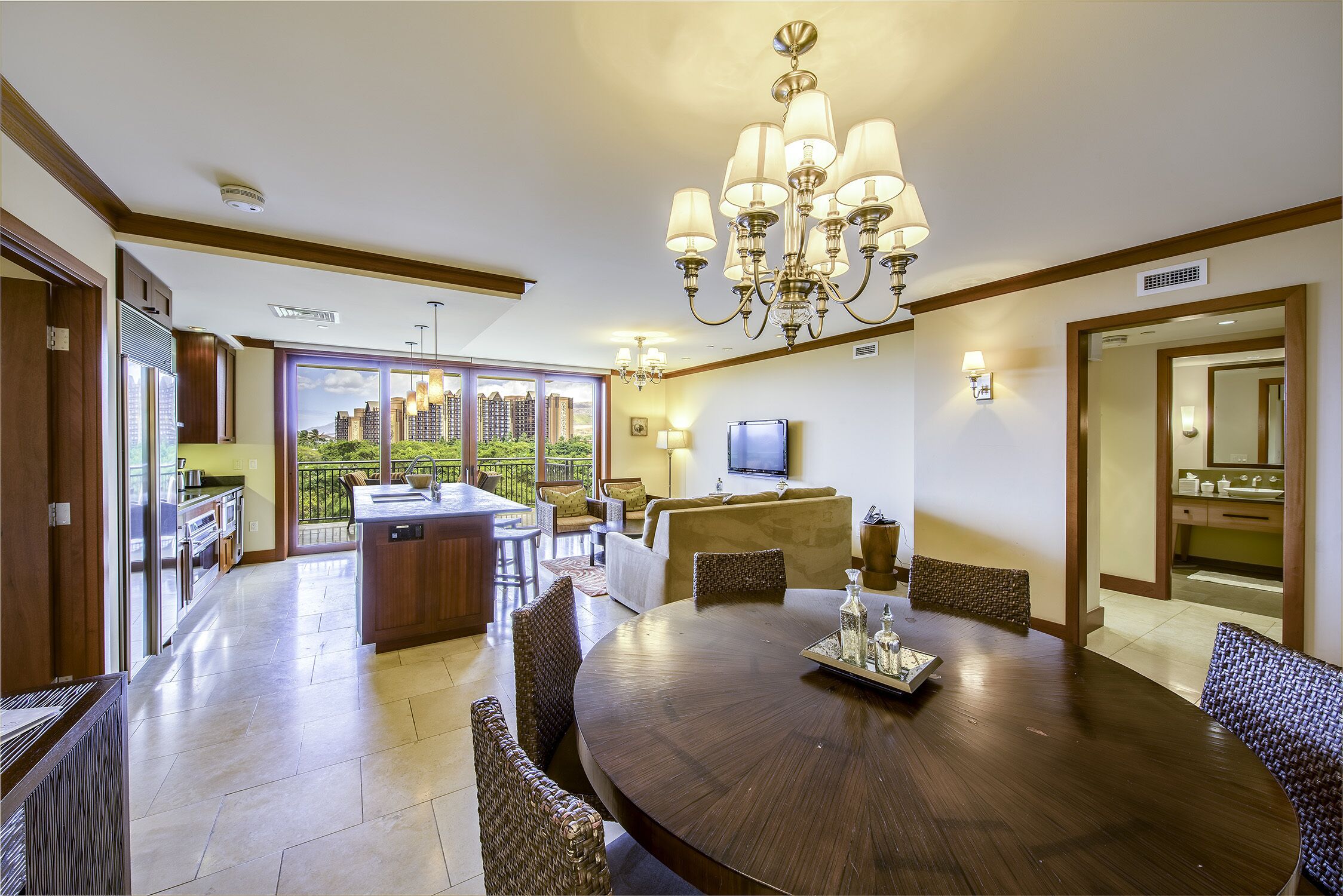 A spacious dining area with a round table, wicker chairs, and a chandelier. A kitchen area with a refrigerator and stove is visible to the left.