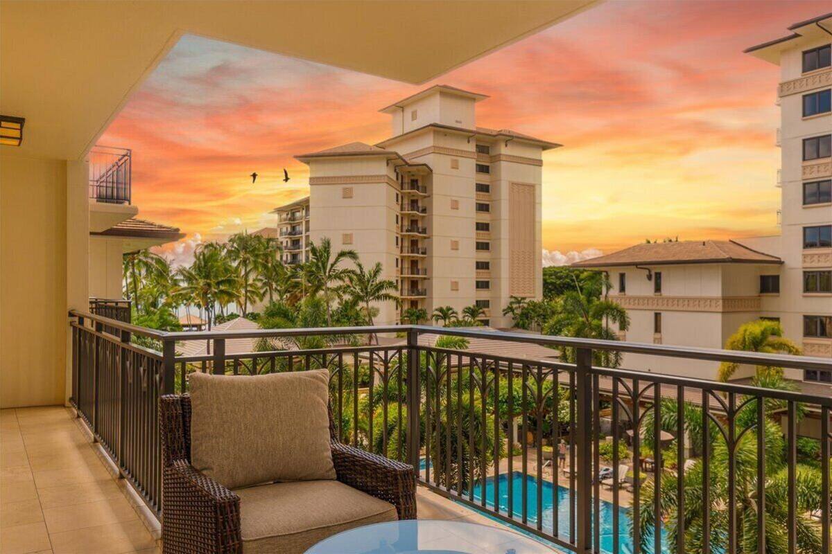 Un balcón con vistas a una piscina y palmeras, con una edificación y un cielo al atardecer.