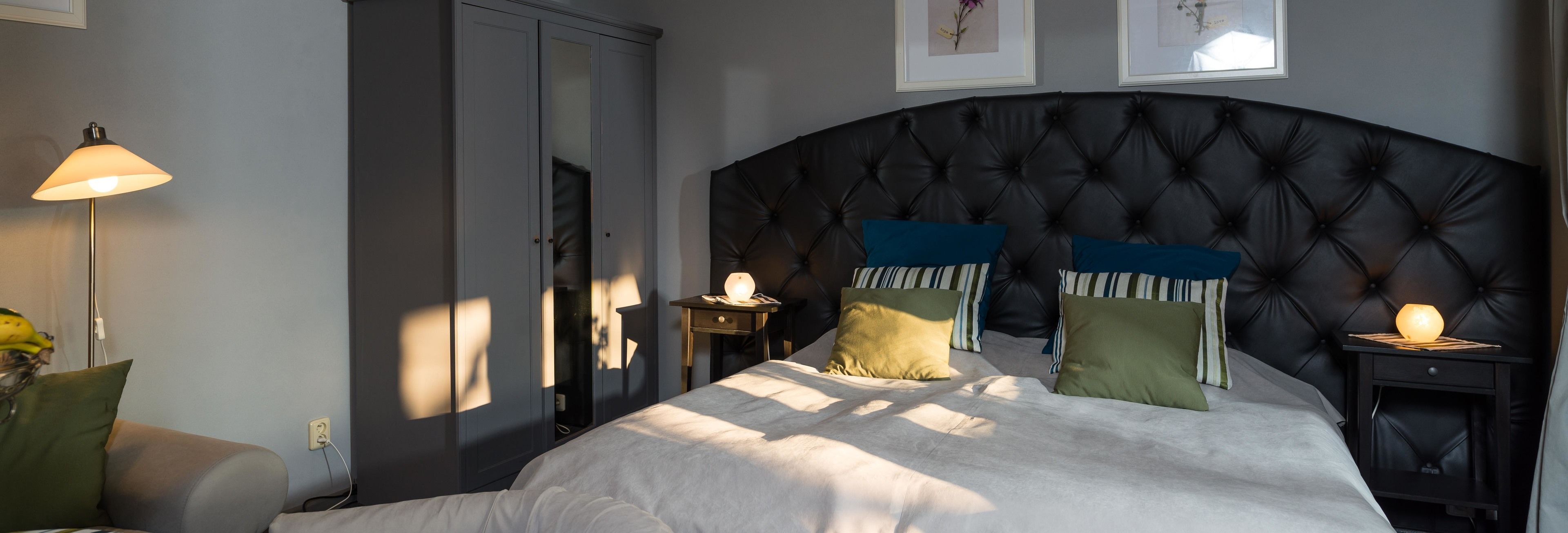 A bedroom with a tufted headboard, a bed with white bedding, two bedside tables with lamps, and a wardrobe.