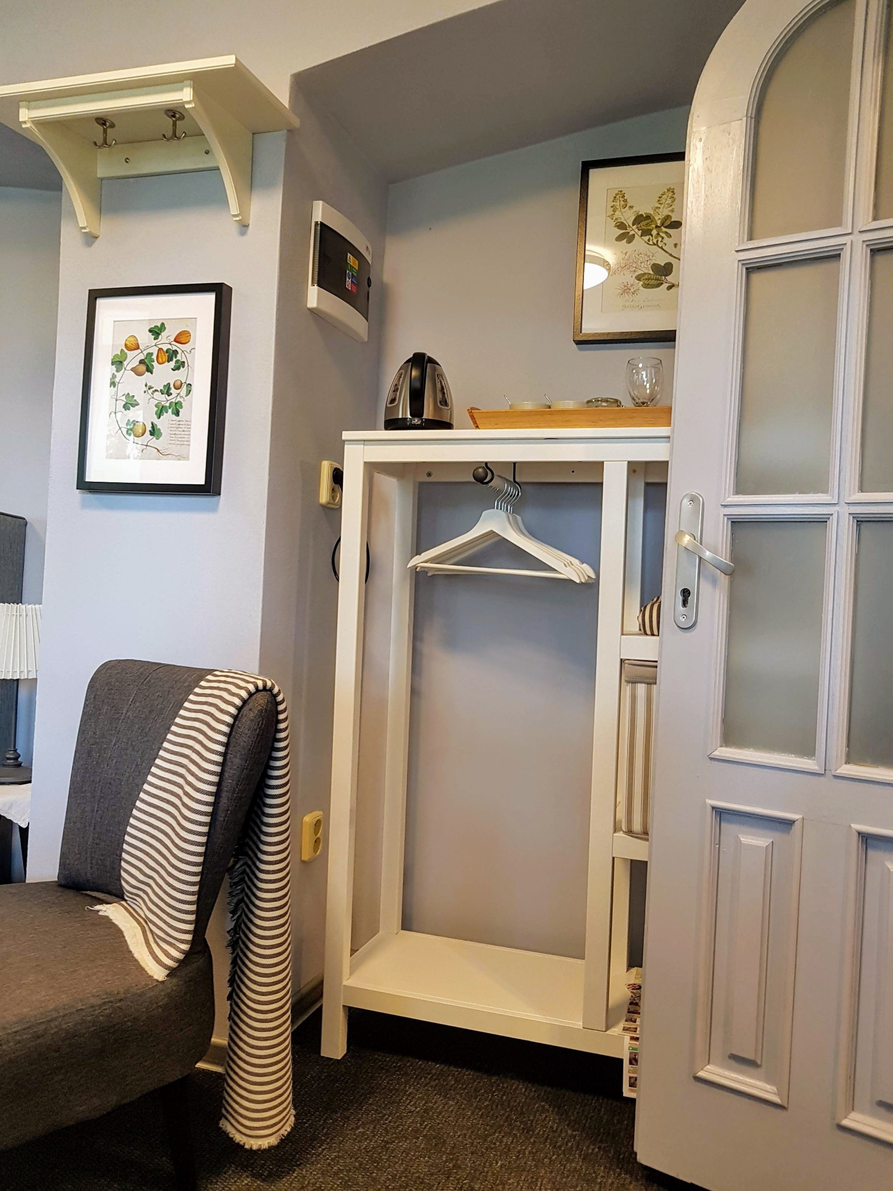 Una habitación con un sofá gris, un perchero blanco, una impresión botánica enmarcada y una puerta con paneles de vidrio esmerilado.