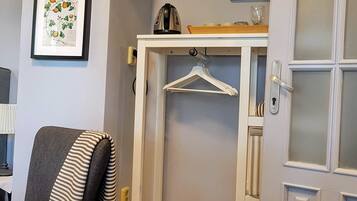 Una habitación con un sofá gris, un perchero blanco, una impresión botánica enmarcada y una puerta con paneles de vidrio esmerilado.