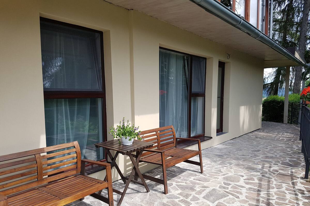 Un patio con suelo de piedra, mobiliario de madera y amplias ventanas con cortinas.