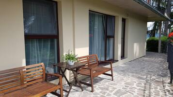 Une terrasse avec un sol en pierre, des meubles en bois et de grandes fenêtres dotées de rideaux.
