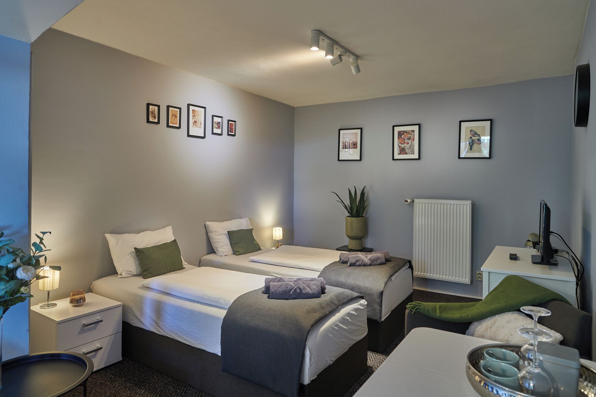 Habitación de hotel con dos camas, un escritorio, un radiador y cuadros en la pared.