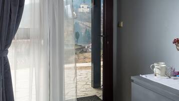 A room with a view of a castle through a window, a vase with fruits, a remote control, and a shadow of a flower on the wall.