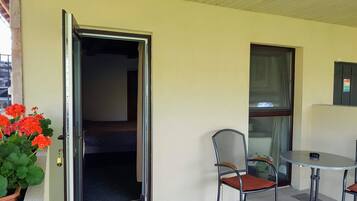 A room with a sliding door, a chair, a small round table, and a potted plant with red flowers.