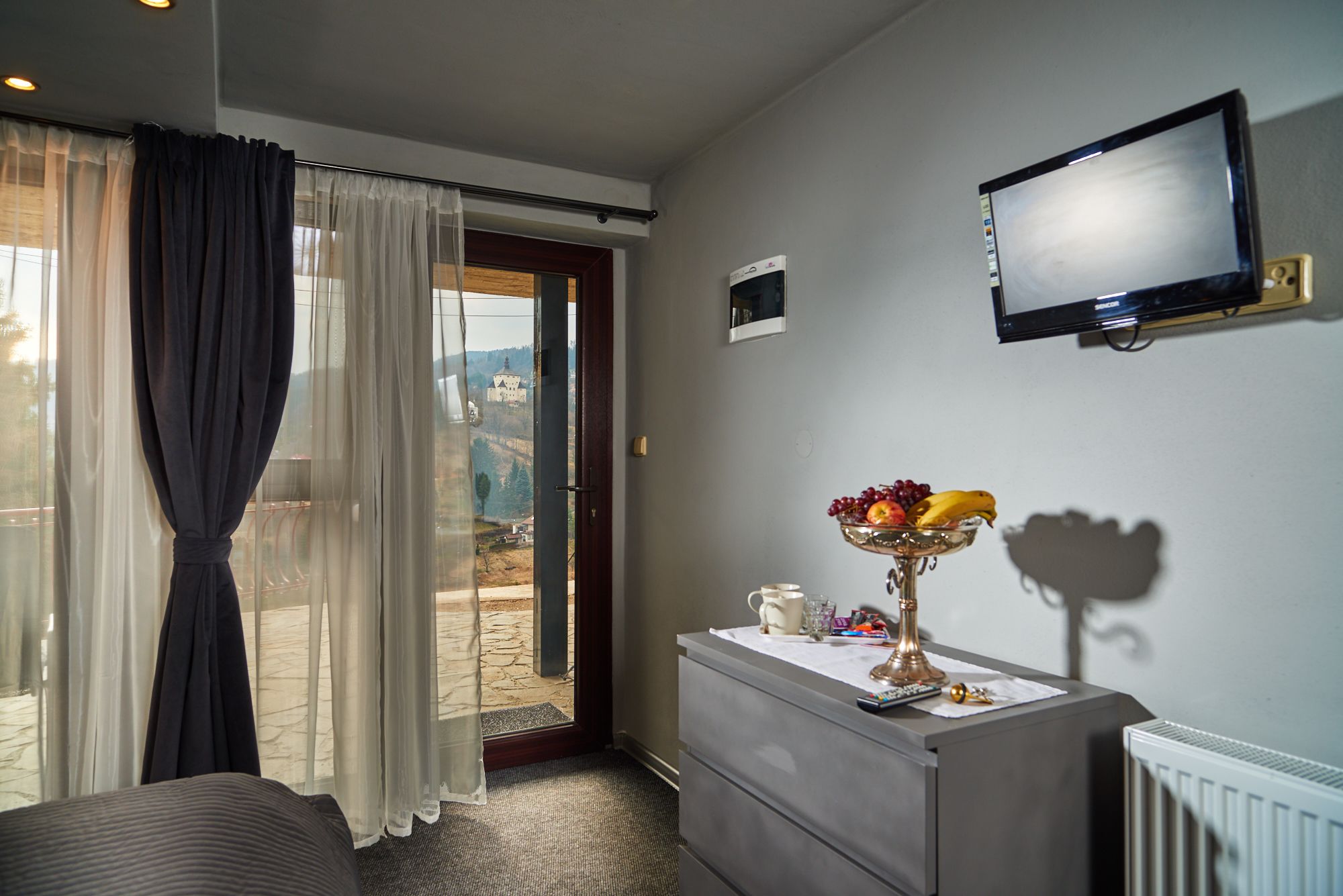Habitación de hotel con cama, cómoda, televisión montada en la pared y vista a un castillo a través de la ventana.
