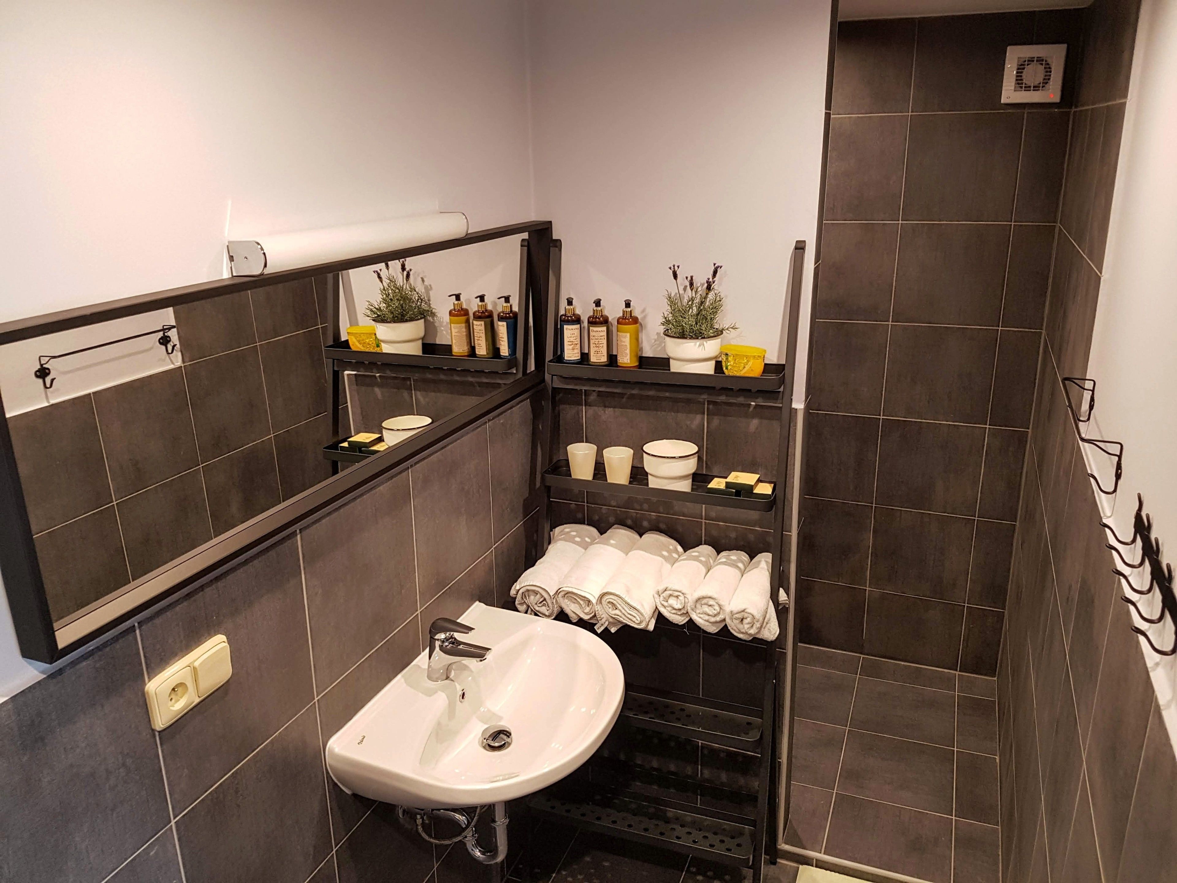 A modern bathroom with a white sink, dark tiled walls, and a shower area.