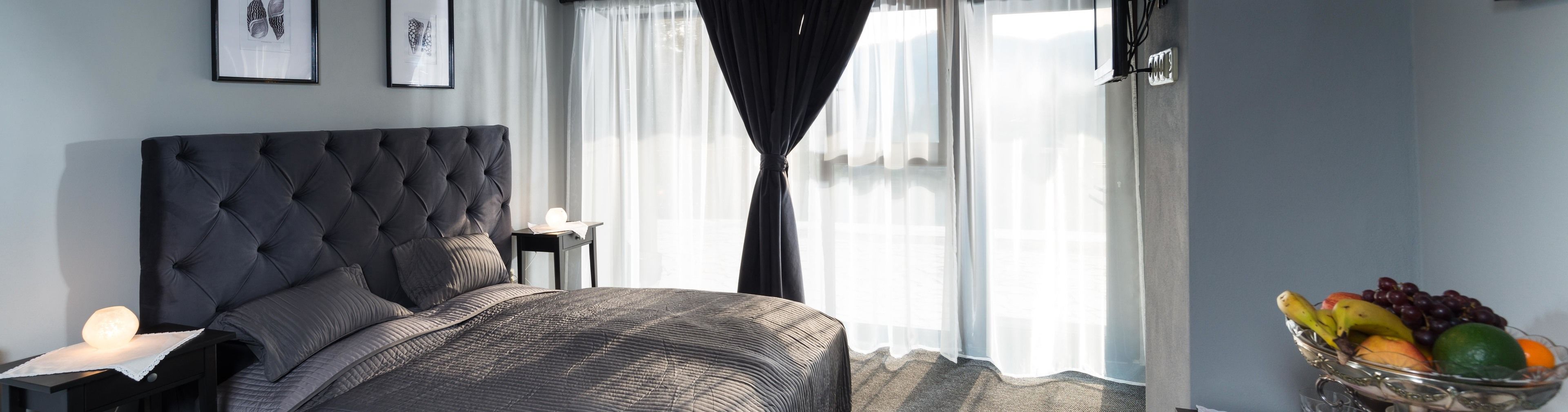 Een slaapkamer met een gestuukt hoofdeinde, een nachtkastje met een lamp, een ingelijste foto aan de muur en een fruitschaal op de vensterbank.
