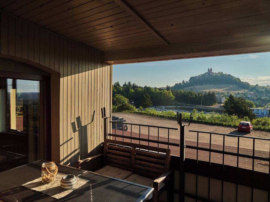 A balcony with a view of a hilltop and a car on the road.