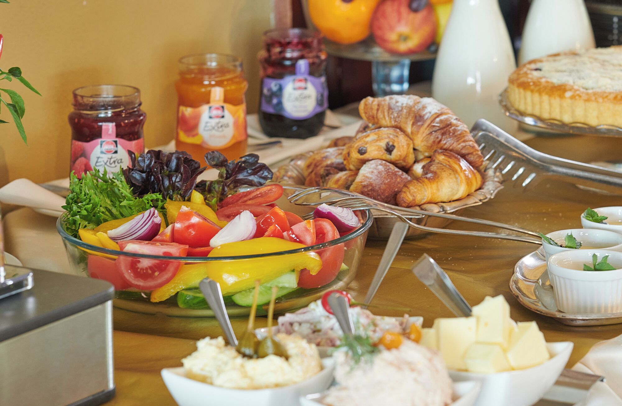 A breakfast buffet with various food items including a salad, croissants, and cheese.