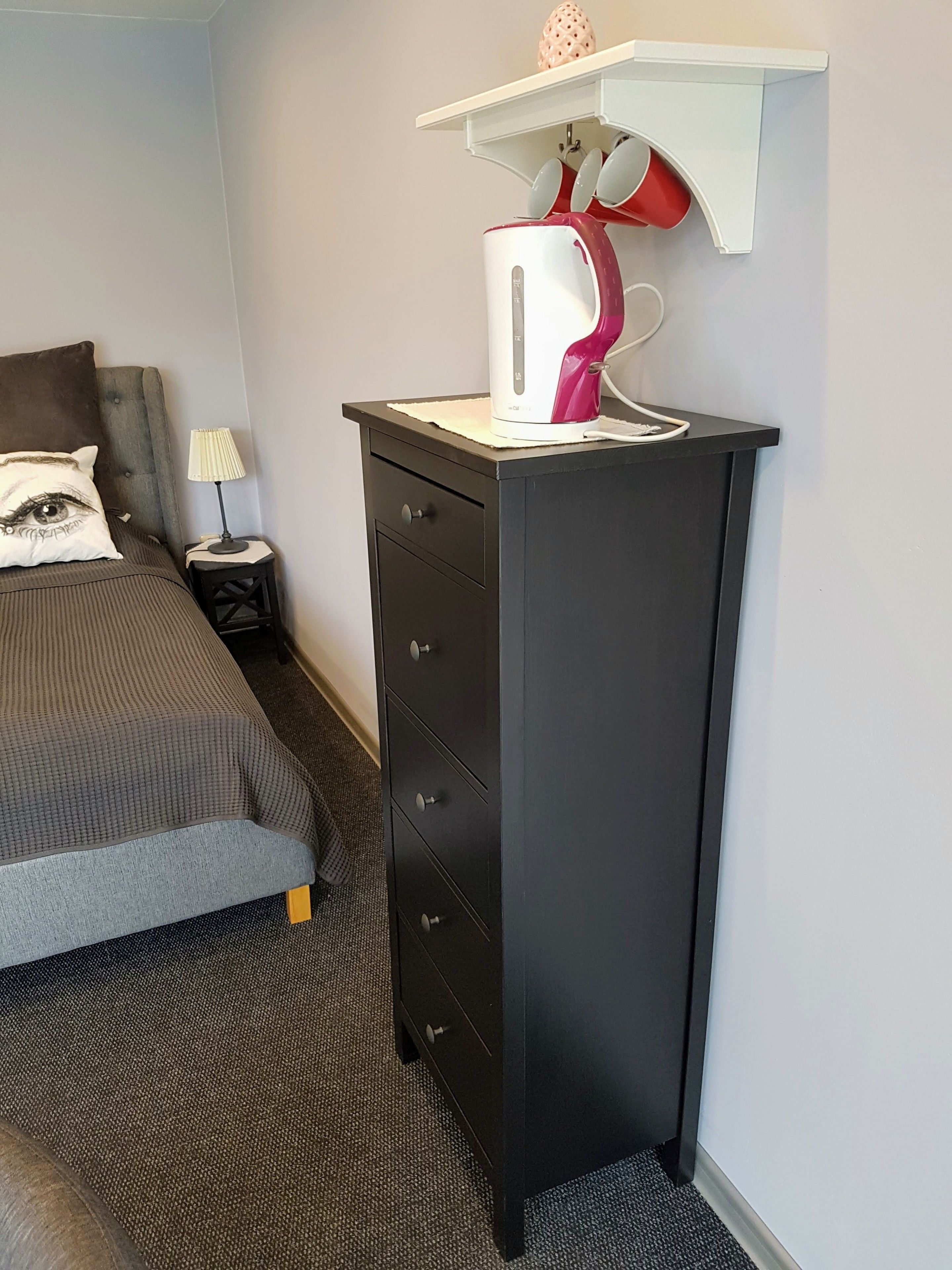 A bedroom with a bed, a dresser, a lamp, and a kettle on the dresser.