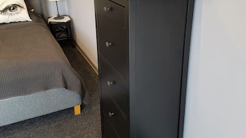 A bedroom with a bed, a dresser, a lamp, and a kettle on the dresser.