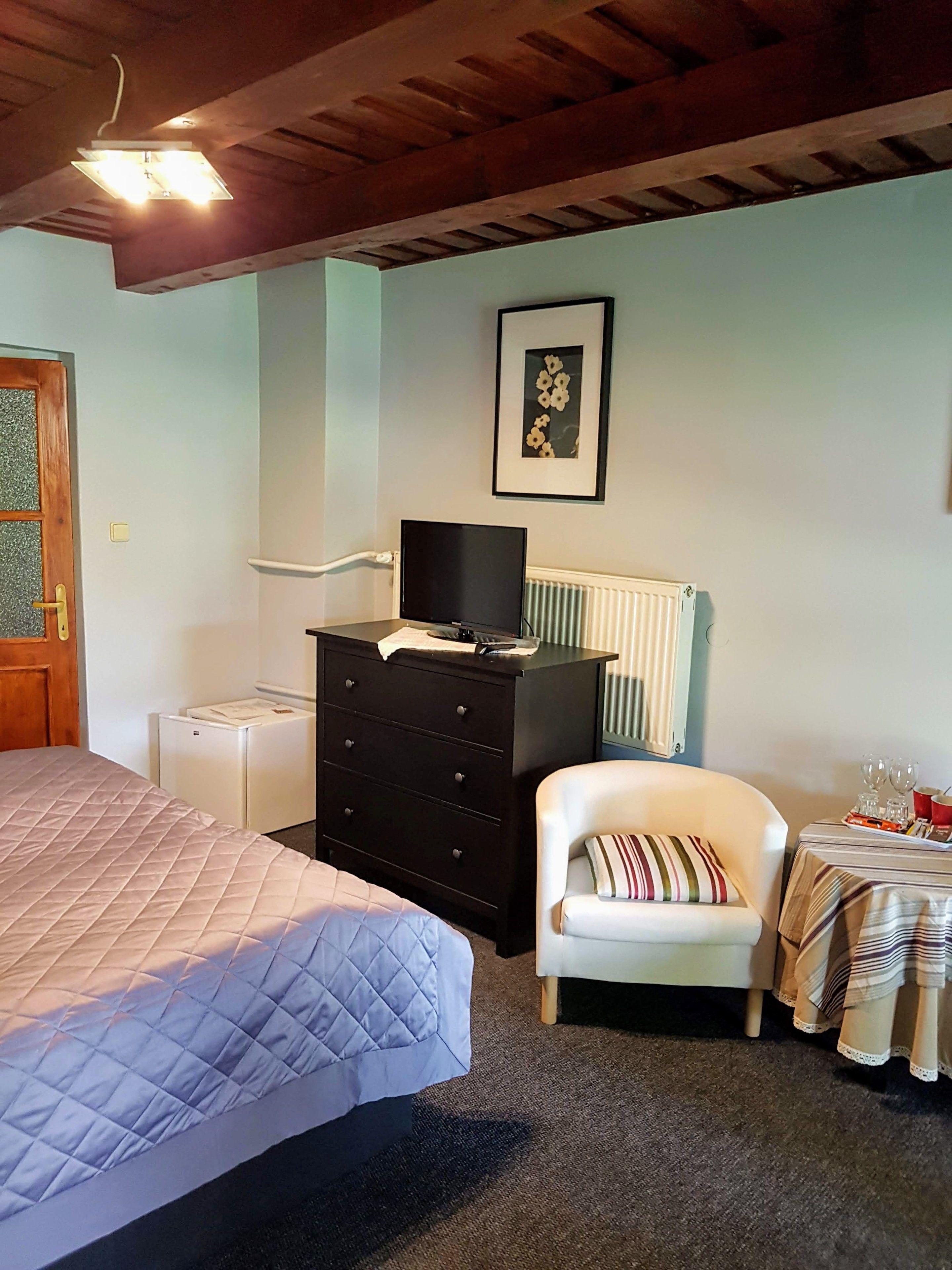 A bedroom with a bed, a dresser, a chair, a table with glasses, and a framed picture on the wall.