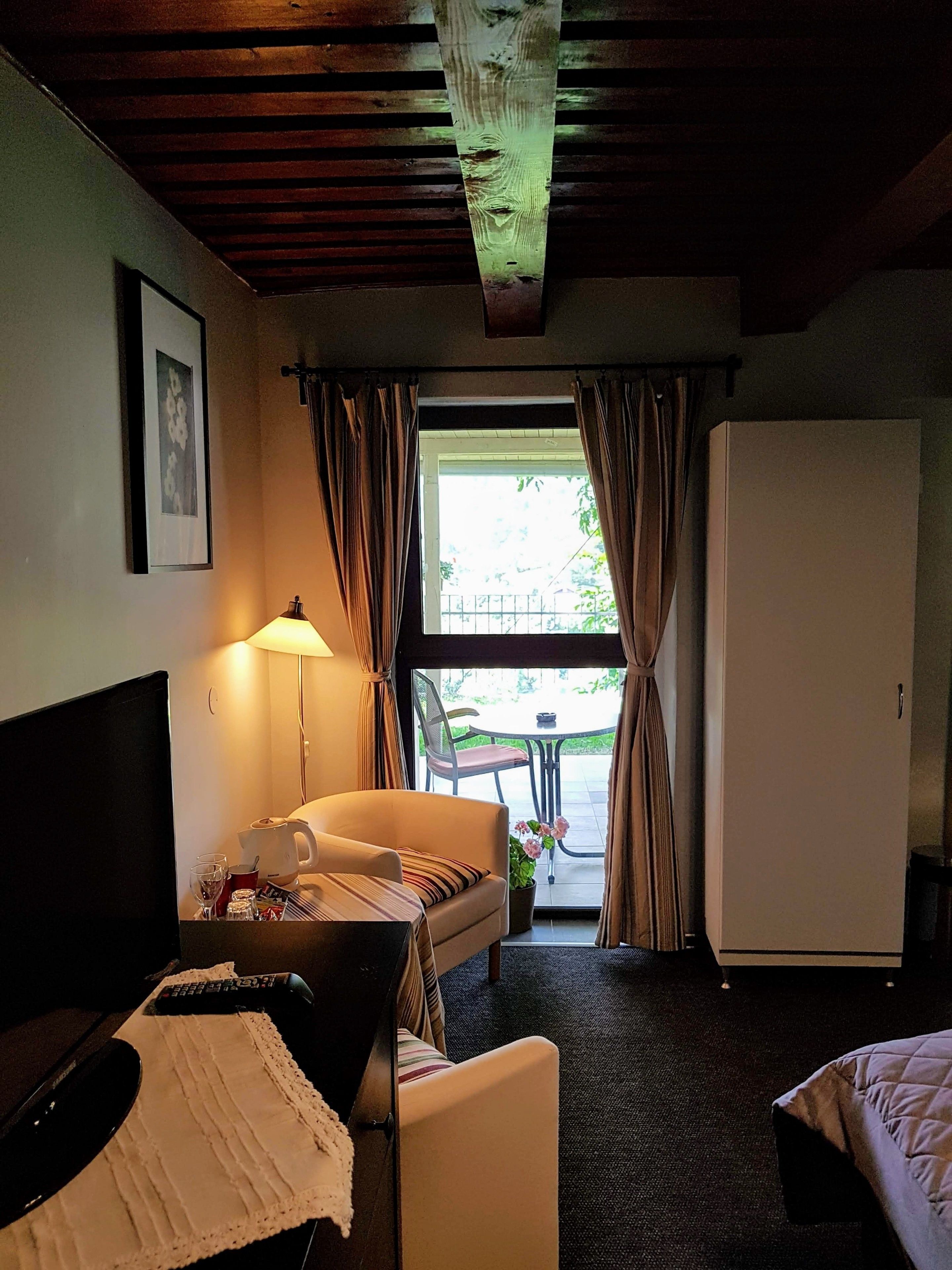 A hotel room with a bed, a desk, a chair, a lamp, a television, a refrigerator, and a window with curtains.