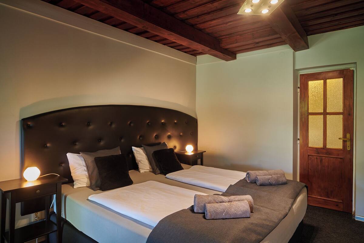 Una cama doble con cabecera capitonada, dos mesitas de noche con lámparas y una puerta de madera con paneles de vidrio esmerilado.