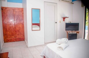 Habitación de hotel con armario de madera, cama con ropa blanca, televisor sobre un mueble de madera y espejo en la pared.