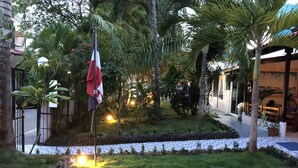 Een binnenplaats met een vlag, palmbomen en een pad dat naar een gebouw leidt.
