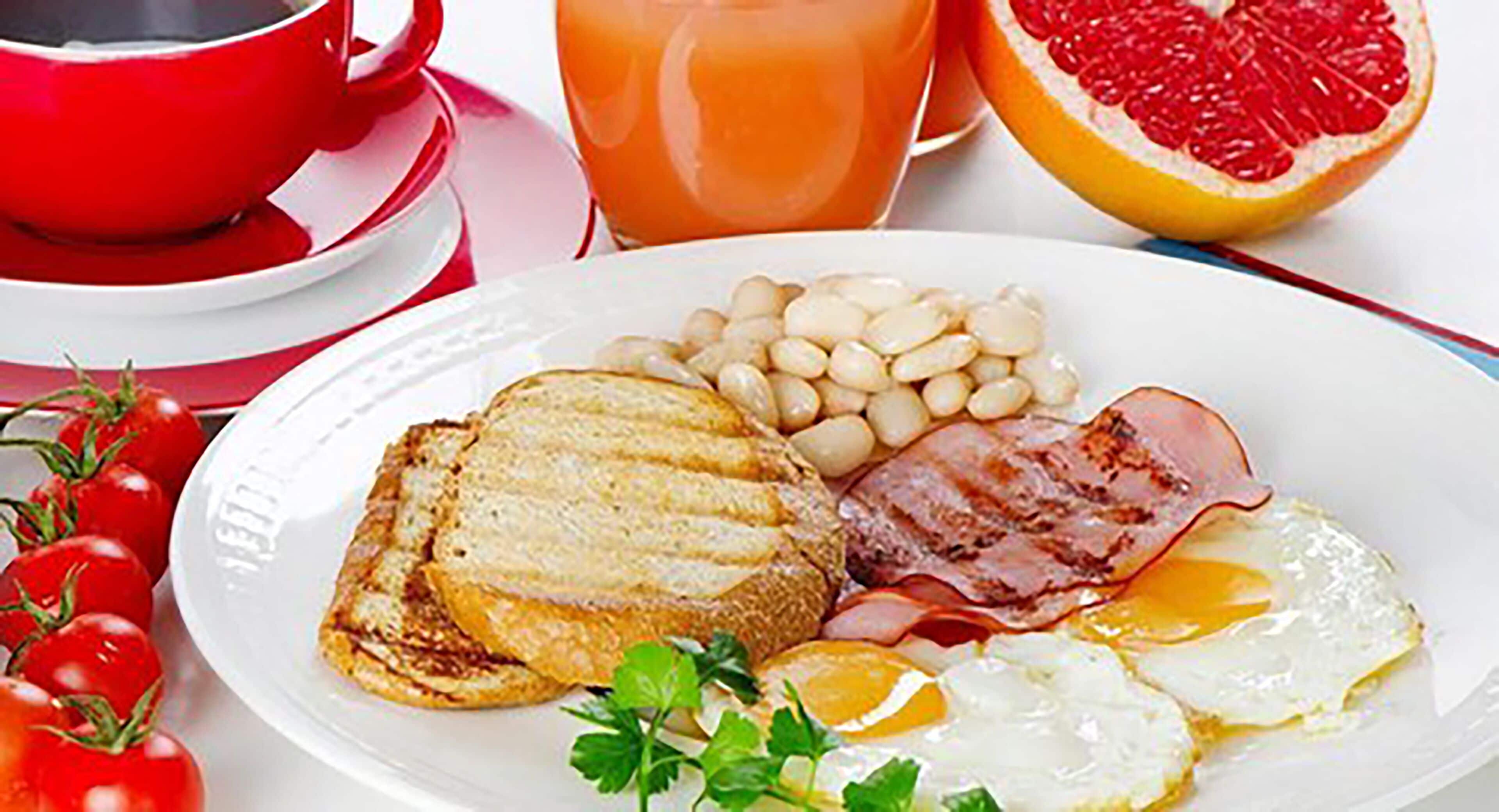Um prato de café da manhã com torradas, feijão, bacon e ovos, acompanhado de um copo de suco de laranja e meia toranja.