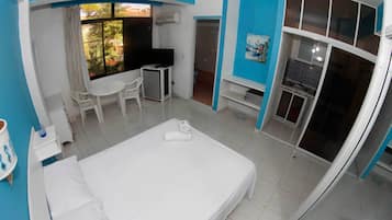 Una habitación de hotel con cama, escritorio, silla, televisión y baño visible a través de una puerta abierta.