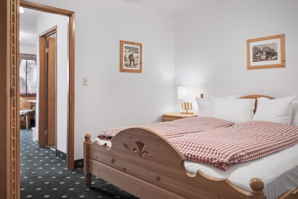 A neatly arranged bedroom with a wooden bed, a bedside table with a lamp, and two framed pictures on the wall.