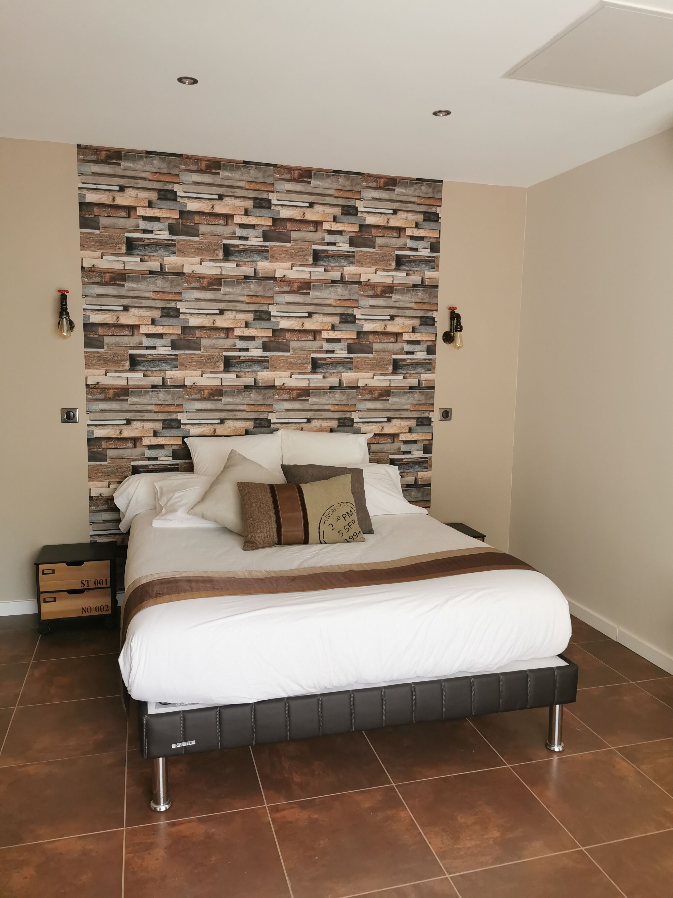 Un dormitorio moderno con cama, mesita de noche, lámpara de pared y panel decorativo.