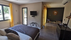Quarto de hotel moderno com cama, escrivaninha, cadeira, televisão e varanda com cortinas amarelas.