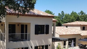 Um edifício de dois andares com varanda, janelas amplas e área de pátio com mobiliário externo.