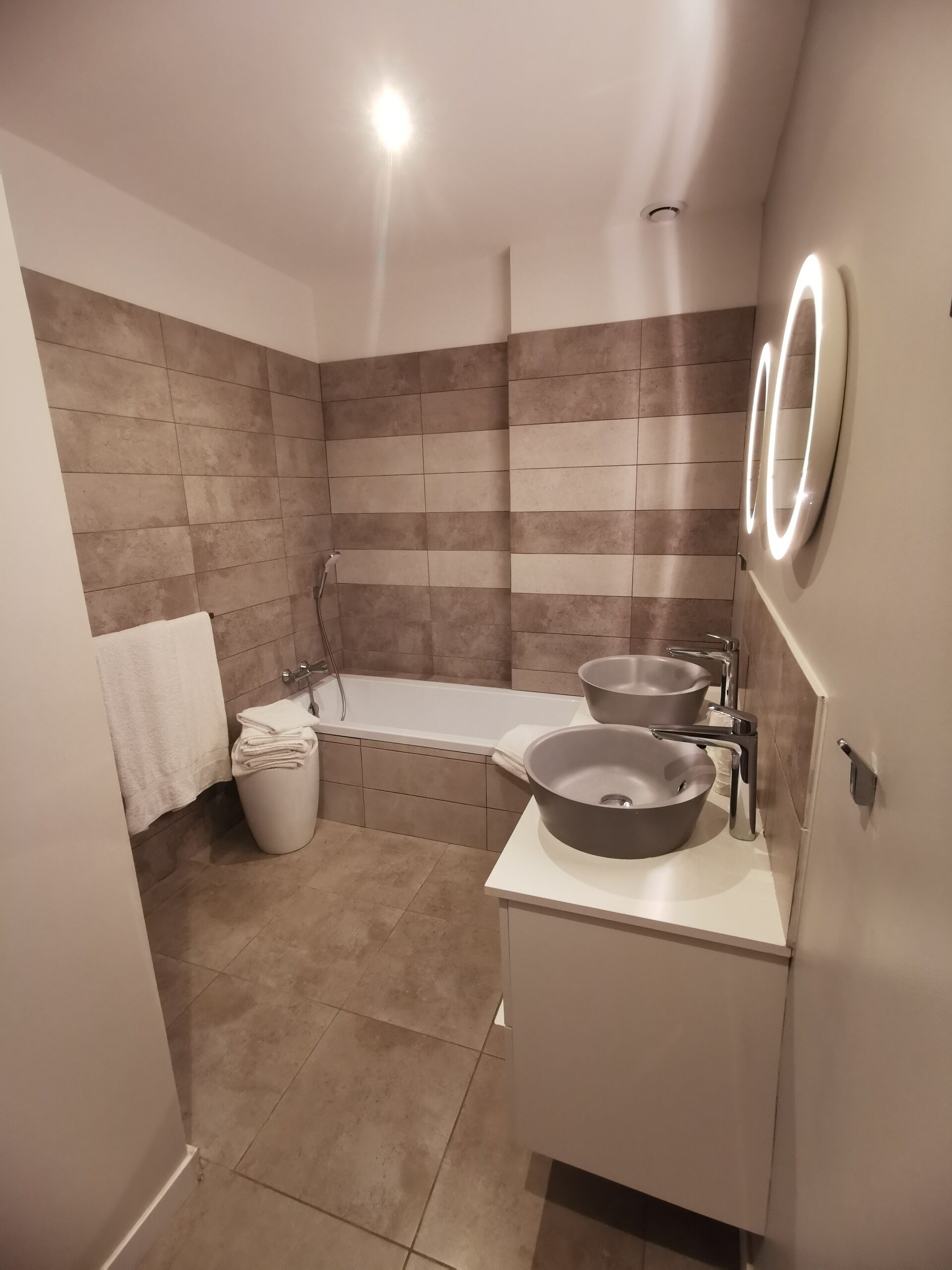 A modern bathroom with a bathtub, two sinks, and a toilet.
