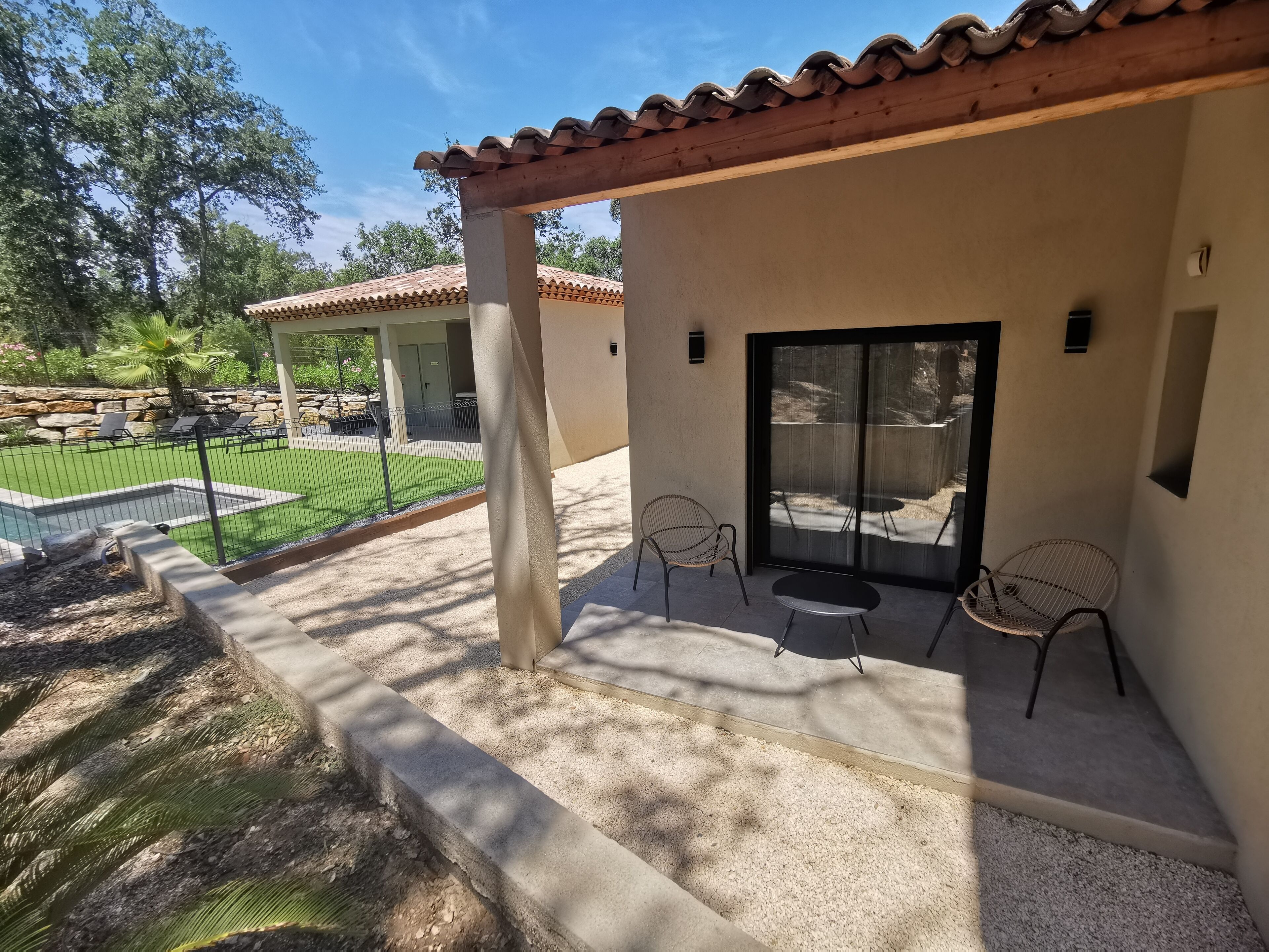 Un patio cubierto con piscina, mobiliario exterior y vistas a un jardín ajardinado.