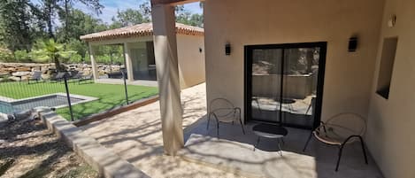 A covered patio area with a pool, outdoor seating, and a view of a landscaped garden.