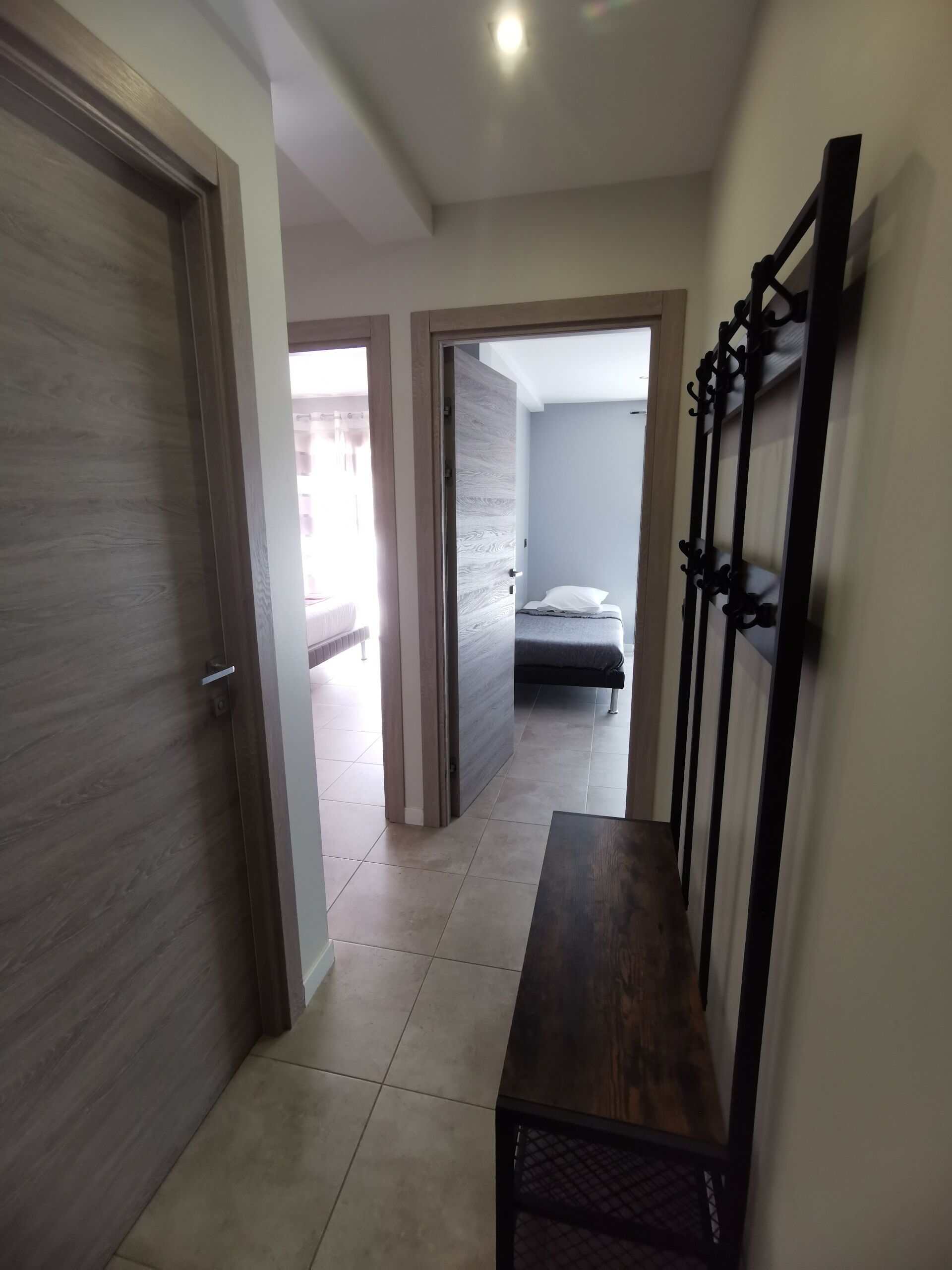 A hallway with a wooden door, a bench, and a bed in the adjacent room.