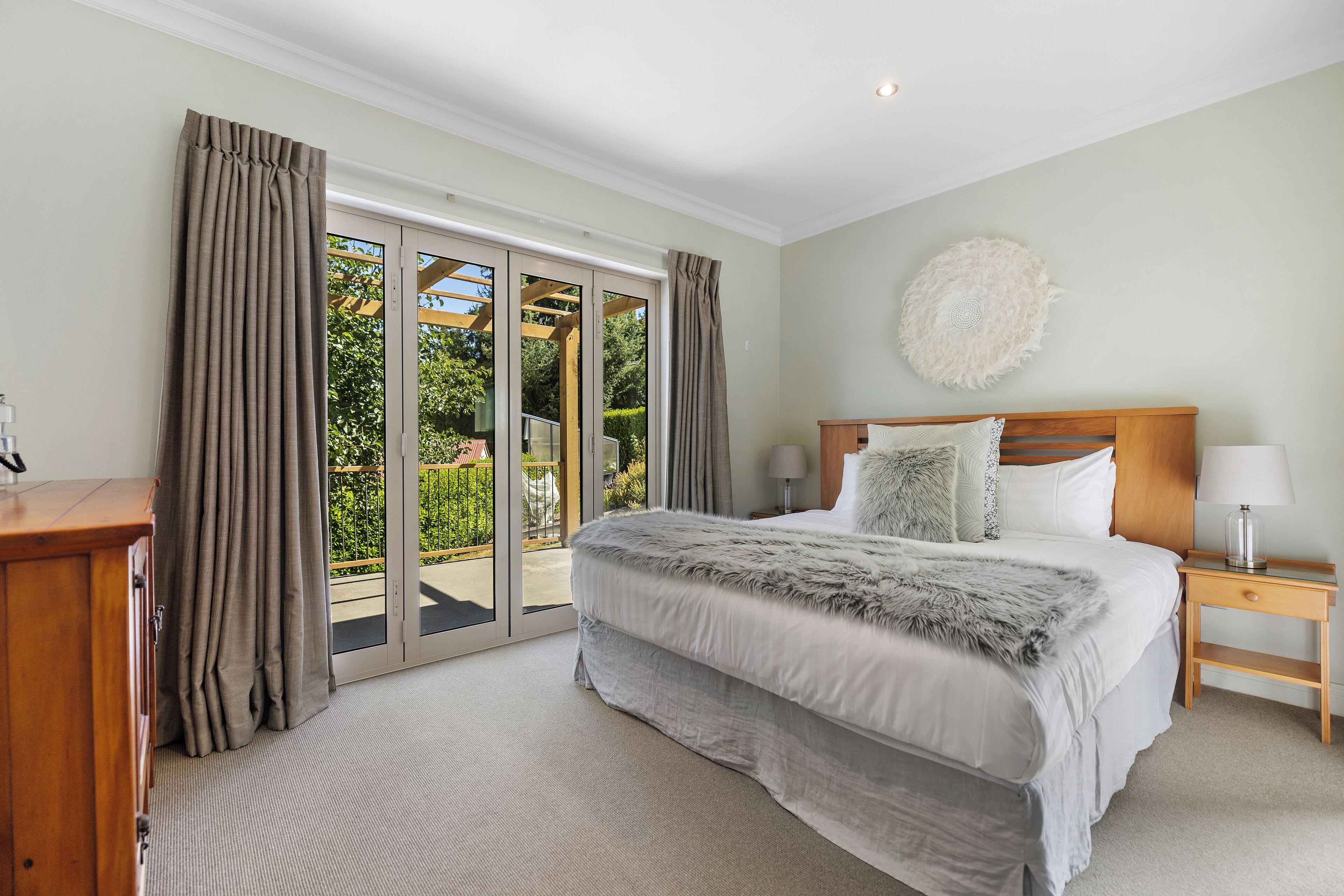 A bedroom with a large bed, a wooden nightstand, a lamp, and a view through a sliding glass door to an outdoor area.