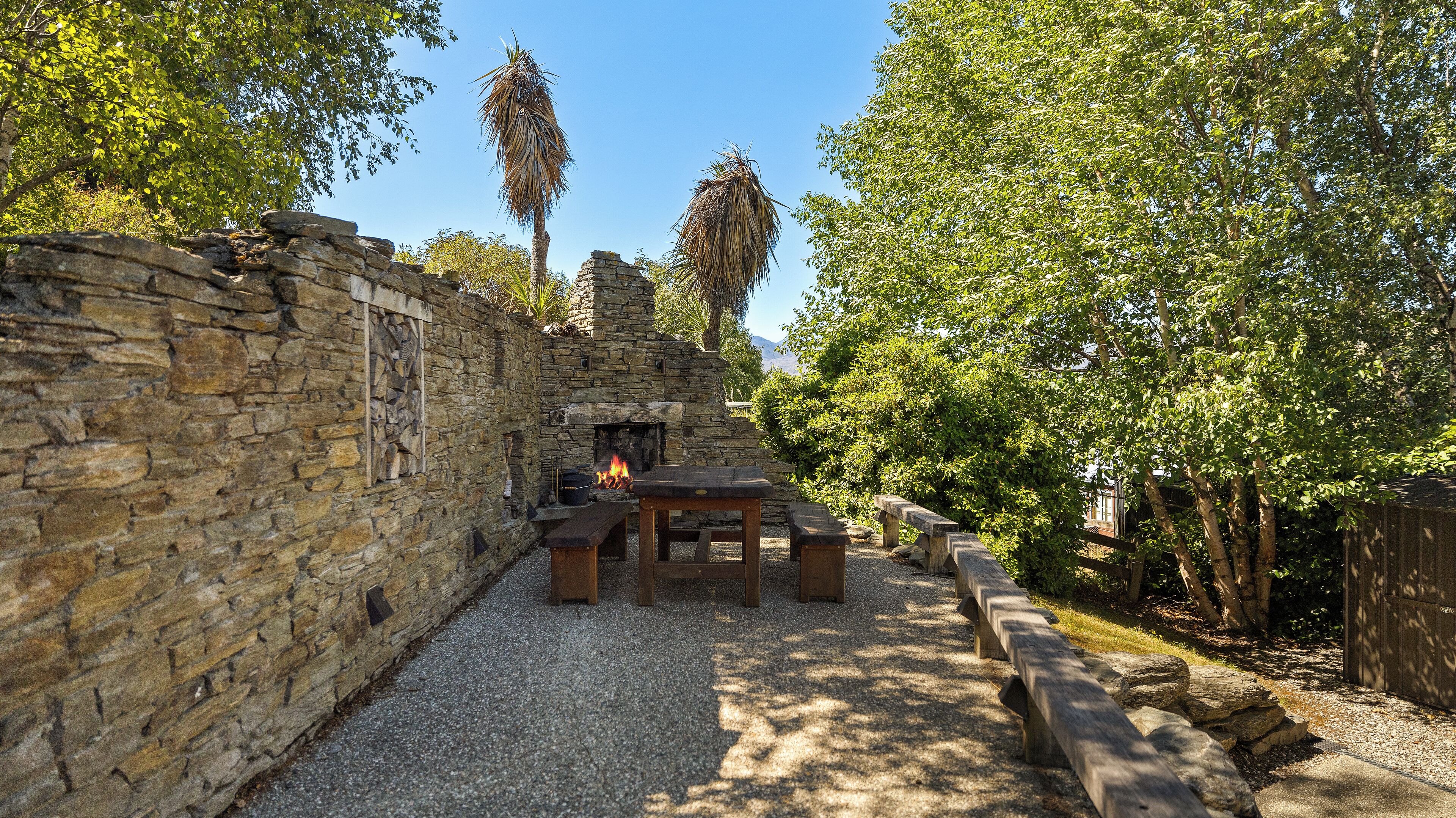 A stone wall with a fire pit and seating area surrounded by trees.