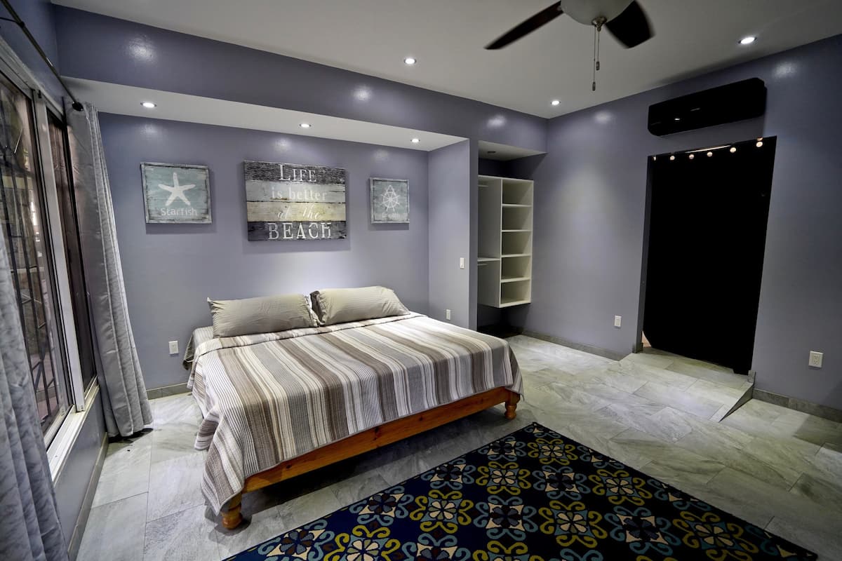 A bedroom with a bed, a ceiling fan, a window with curtains, and a wall with decorative items.