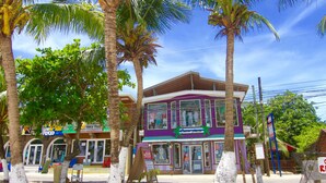 Un edificio de dos pisos con fachada morada, un letrero que dice 'Coco Juice' y palmeras en la parte delantera.