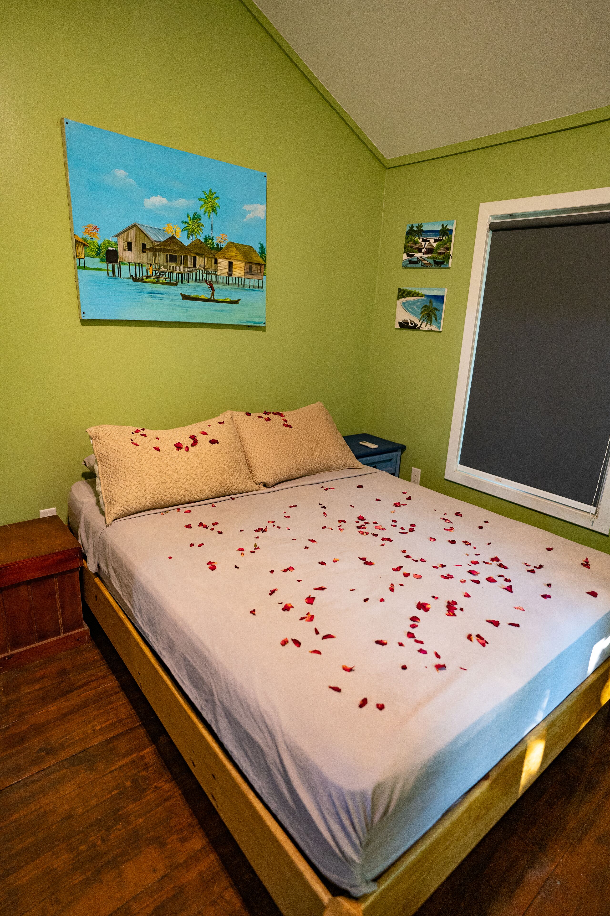 Un dormitorio con cama, paredes verdes, un cuadro y una ventana.