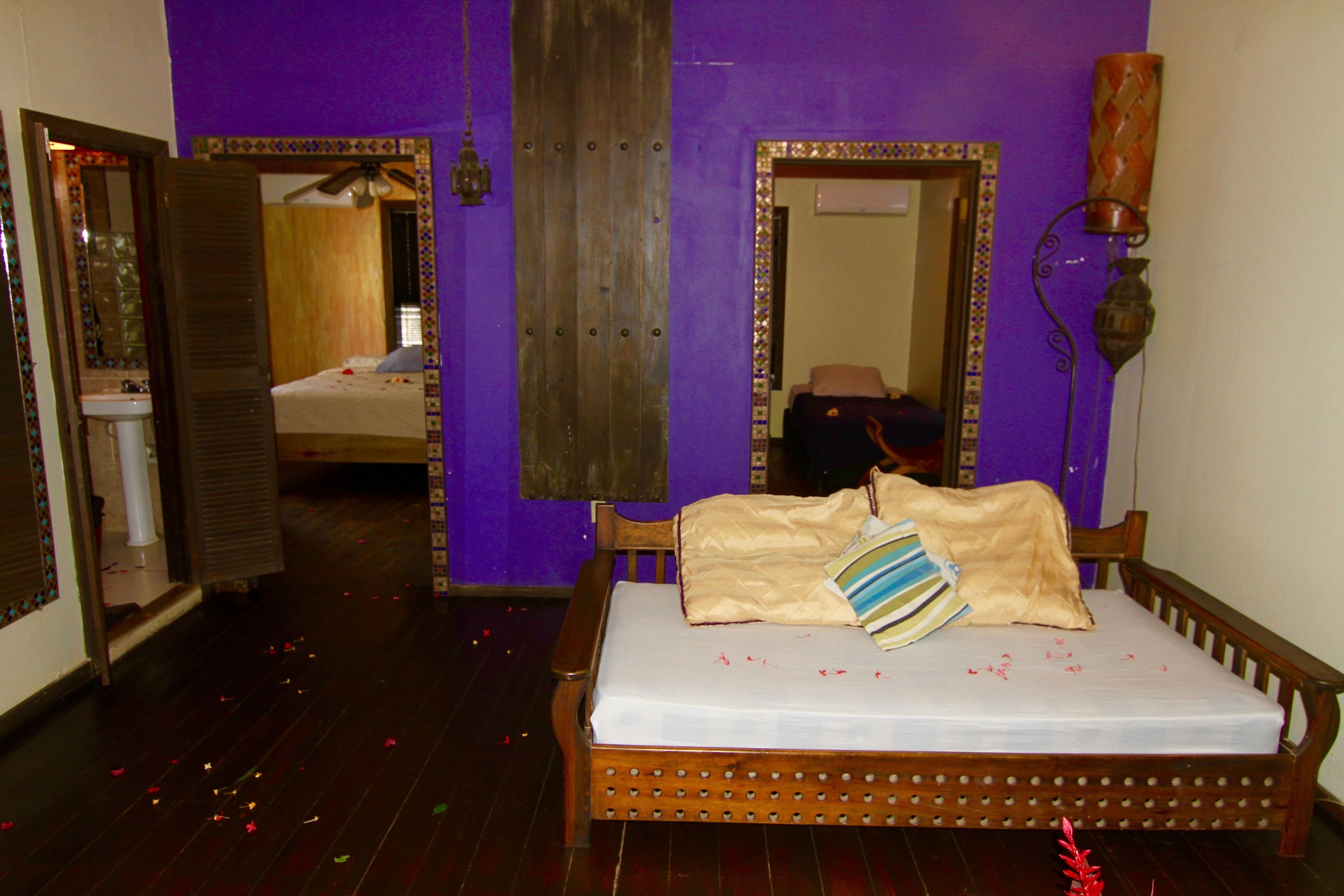 Quarto com uma cama de madeira, um espelho e um banheiro visível por uma porta aberta.