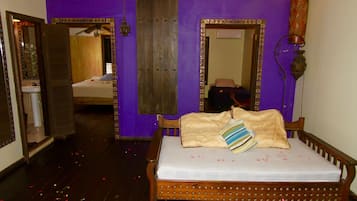 Une chambre avec un lit en bois, un miroir et une salle de bain visible à travers une porte ouverte.