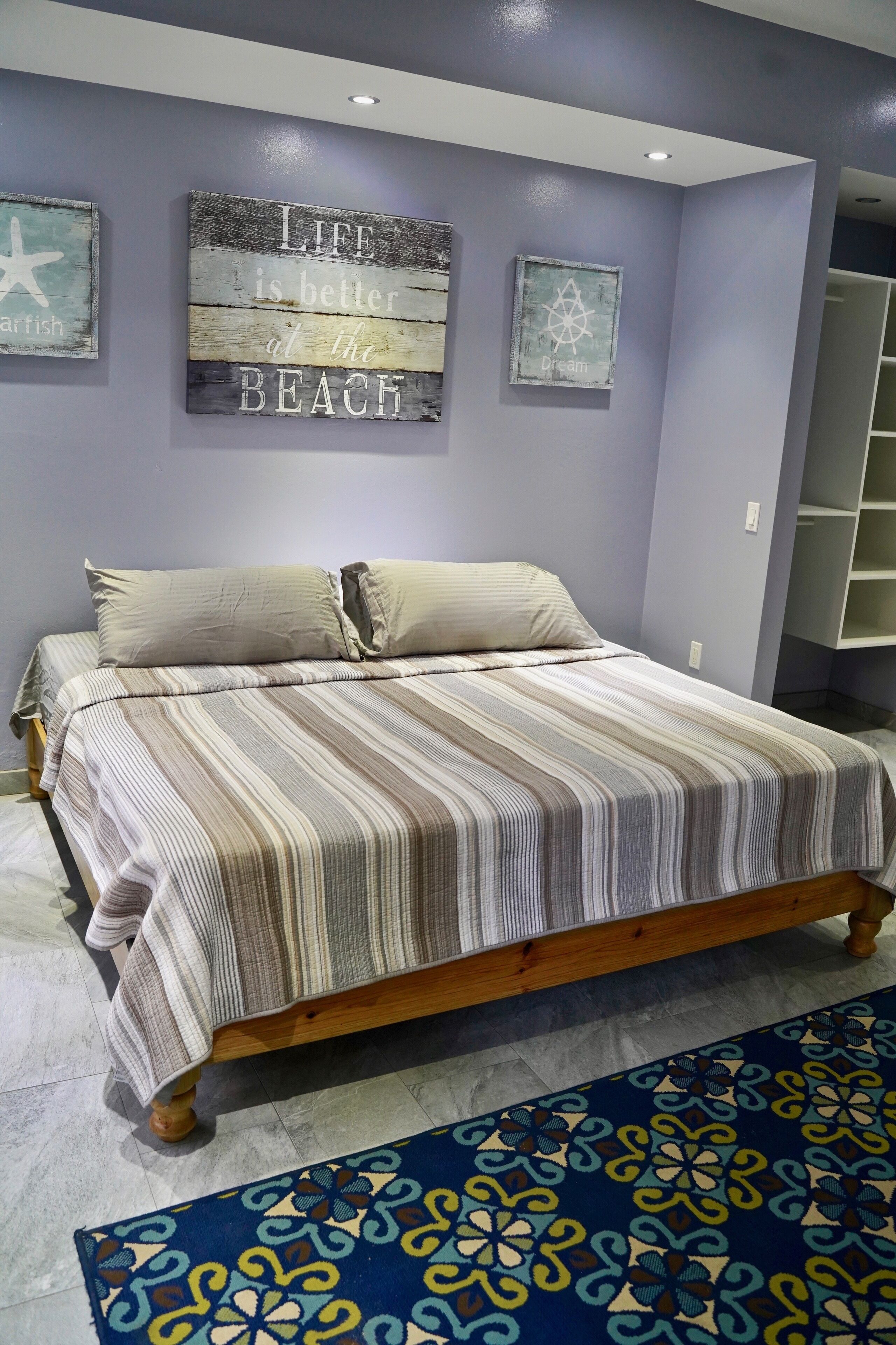 Een slaapkamer met een bed, een blauw tapijt met patroon, en drie kunstwerken aan de muur.