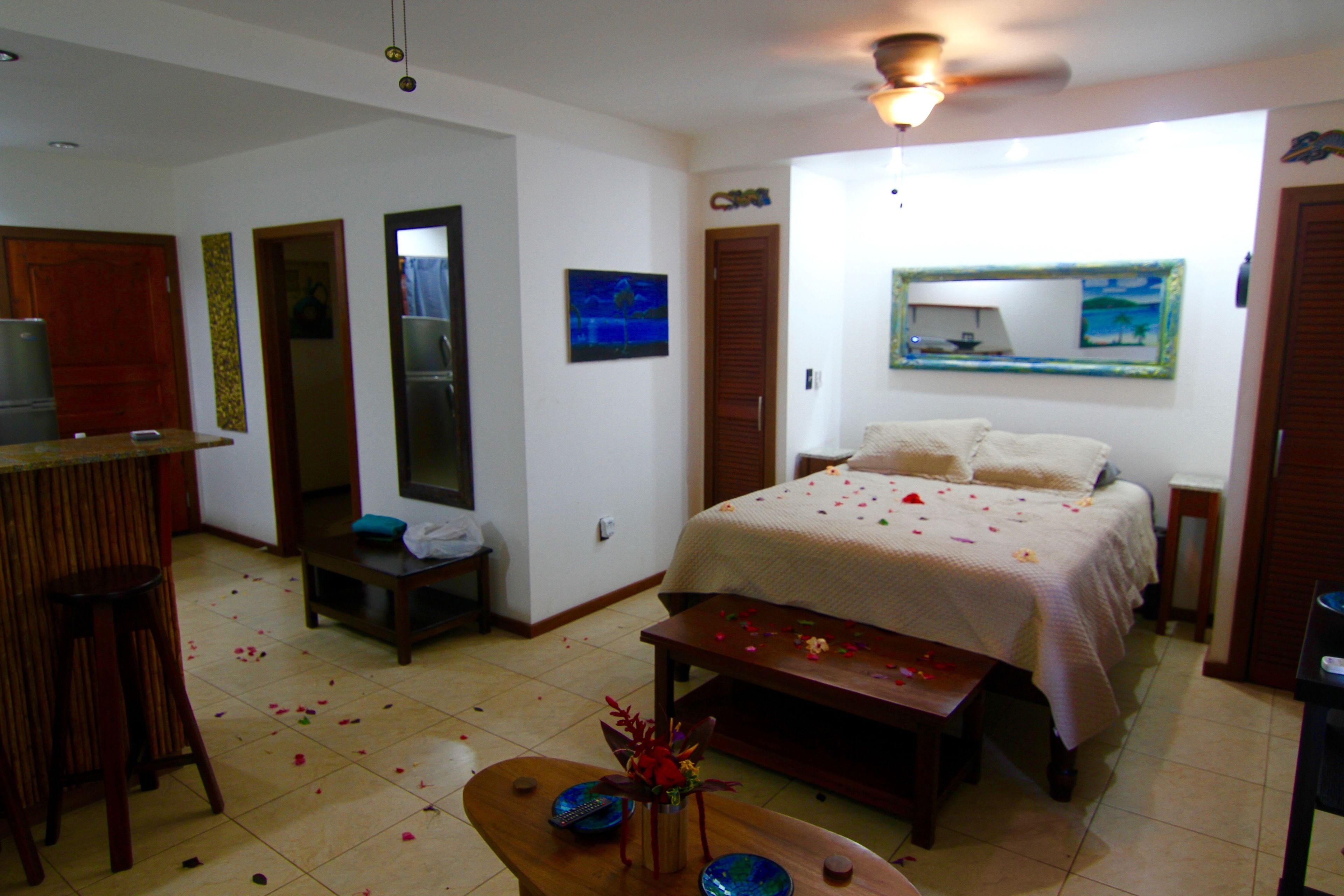 A hotel room with a bed, a desk, a chair, a small table, and a TV.