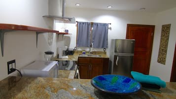 Una cocina compacta con encimeras de granito, un refrigerador de acero inoxidable y un tazón decorativo azul.