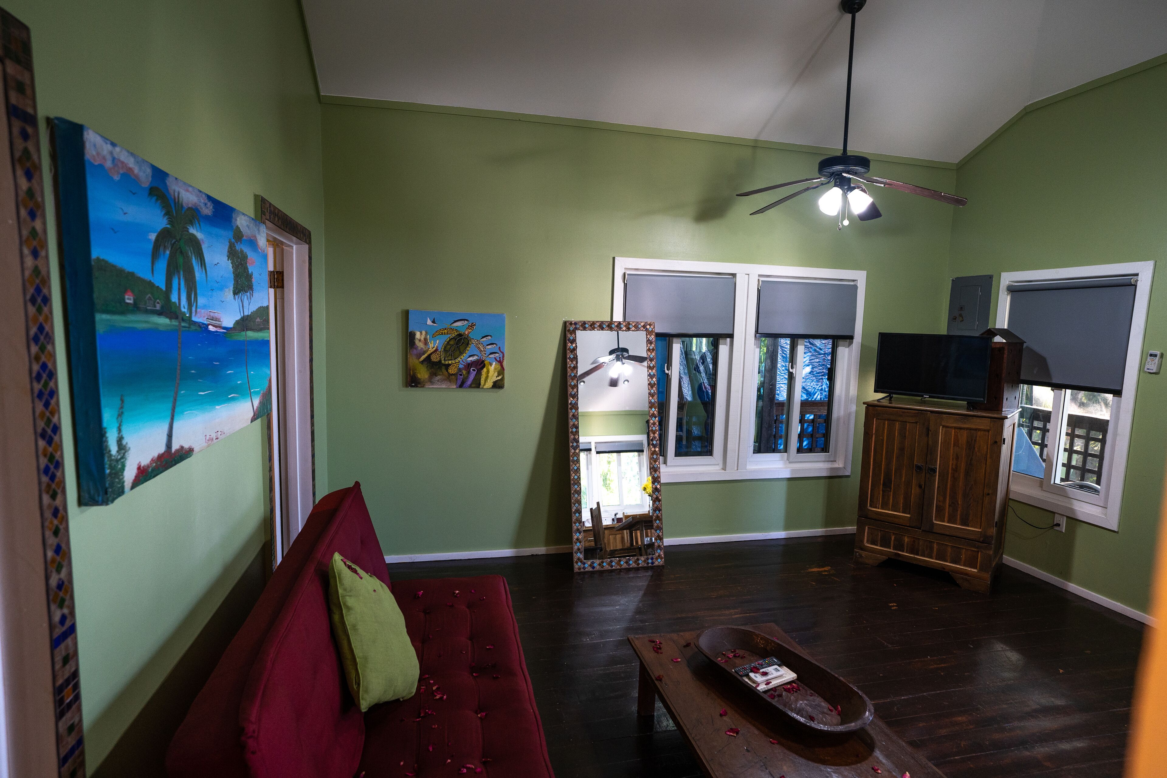 Un salon avec un canapé rouge, une table basse en bois, un ventilateur de plafond et un grand miroir.