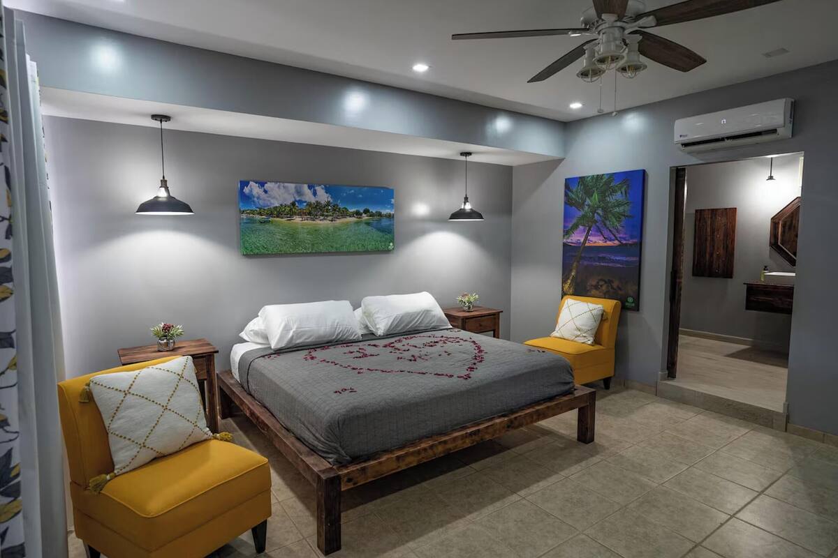 A bedroom with a bed, two bedside tables, a ceiling fan, and two wall-mounted pendant lights.