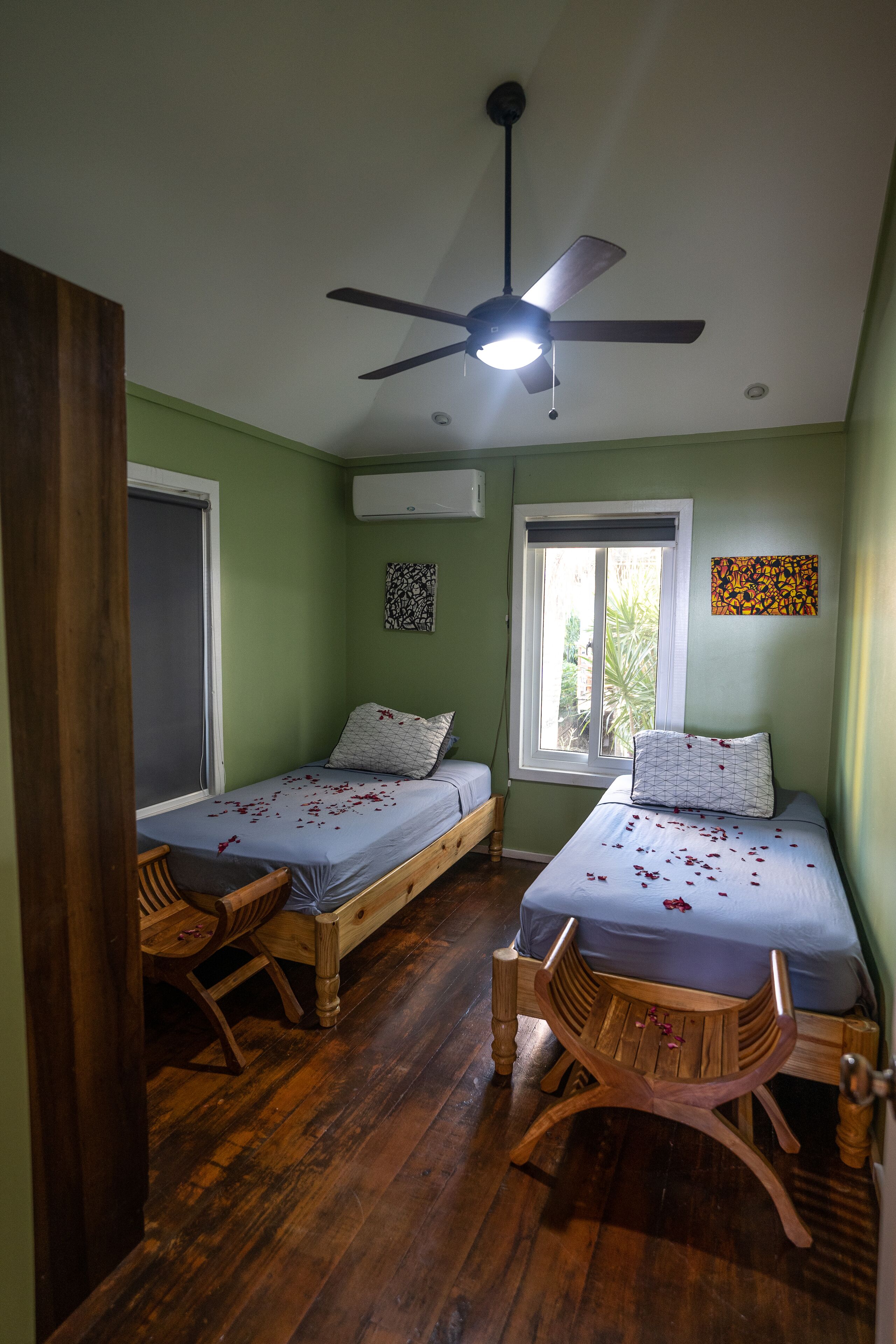 Una habitación con dos camas individuales, ventilador de techo, ventana con vistas y suelo de madera.