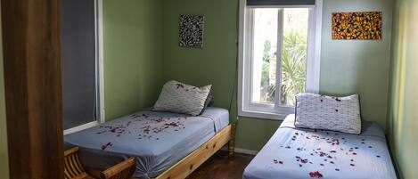 Una habitación con dos camas individuales, ventilador de techo, ventana con vistas y suelo de madera.