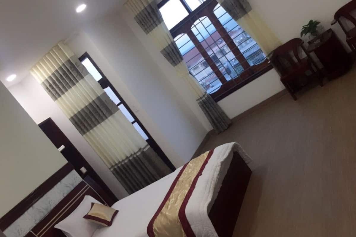 Une chambre d’hôtel comprenant un lit, un bureau, une chaise, une fenêtre avec des rideaux et une vue sur les bâtiments environnants.